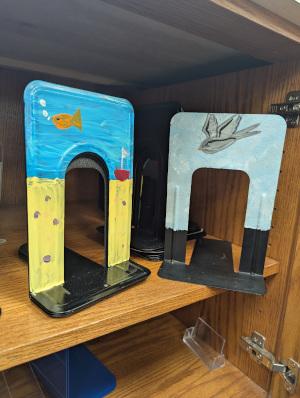 Two bookends painted with undersea scenes sitting on a shelf