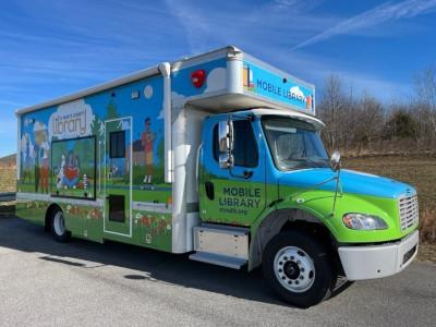 A large truck with an outdoor scene painted on the side, including people walking, talking, reading, and playing