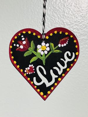 A painted heart with two red flowers and the word love, hanging on a black and white string