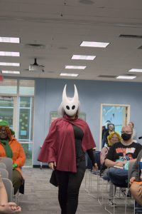 A cosplayer wearing a Hollow Knight mask and a red cape