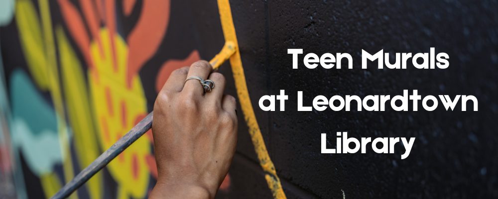 A hand painting a yellow line. Teen Murals at Leonardtown Library