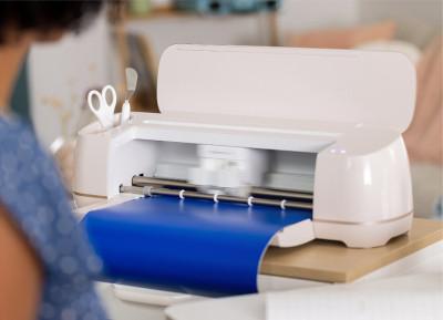 A Cricut cutting machine, open with blue vinyl being fed into it