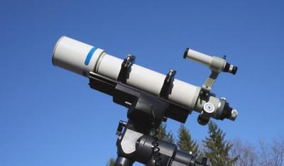 A large white telescope set up outside during the day with a clear blue sky in the background