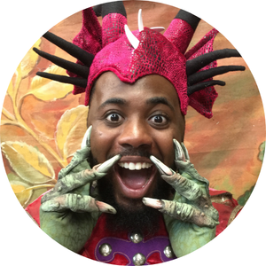 A grinning Black man wearing a bright pink & green dinosaur costume.