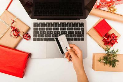 A hand holds a credit card over a laptop, surrounding by wrapped gifts