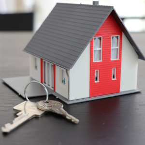A small model of an a frame house sits on a table. A keyring with two keys sits next to it.
