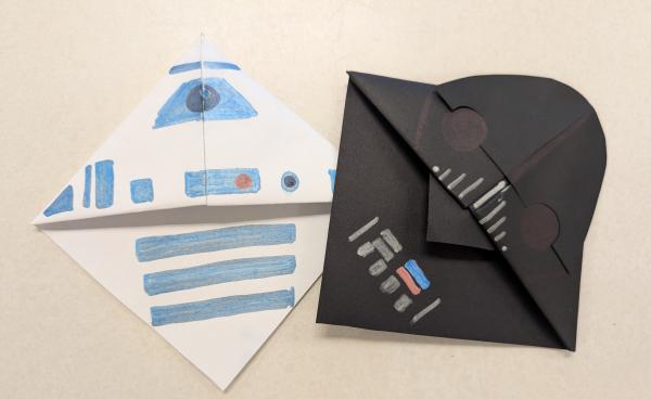 Two corner bookmarks made of paper and decorated to look like Darth Vader's helmet and a droid