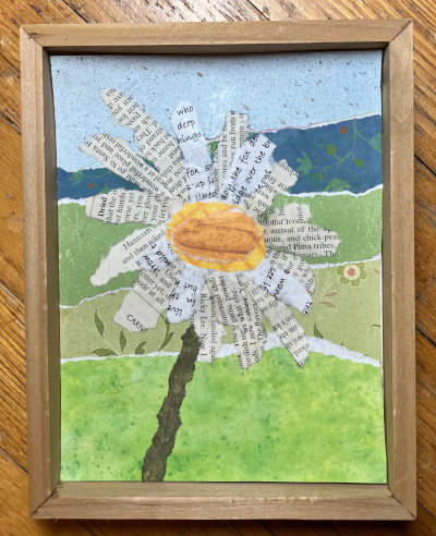 A framed collage of a flower with petals made from newspaper and a background of watercolor-painted paper