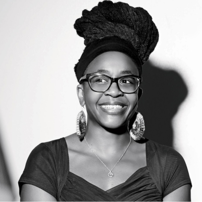 Headshot of a Black woman wearing glasses and large earrings with her hair on top of her head above a headband