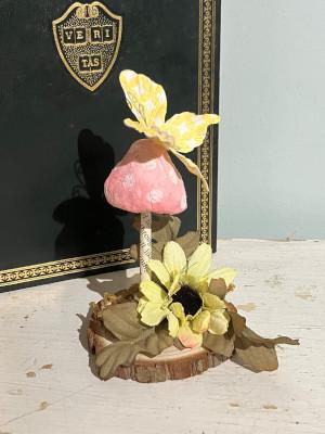 A toadstool with a yellow flower at its base and a yellow butterfly perched atop it